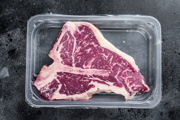 T-bon raw beef steak in vacuum packaging. Black background. Top view