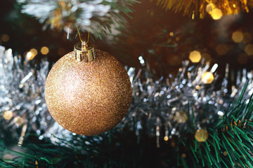 Obraz na płótnie Canvas Golden ball on decorated Christmas tree with blurred lights bokeh. Selective focus. Holiday card with decorations for the New Year's Eve