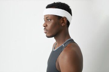 Profile studio shot of young attractive Afro man wearing headband and tank top, posing with concentrated and focused face expression, trying to calm himself down and settle in for sports victory - Powered by Adobe