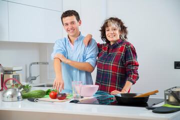 pareja joven sonriente haciendo una masa en un bol rosa, en una cocina blanca con placa de...