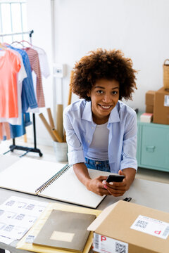 Young female fashion designer with smart phone at studio