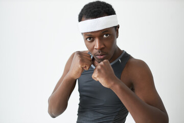Studio image of dark-skinned athlete holding fists in front of him in defensive stance, looking at camera with serious, concentrated face. People, sport, competition. Body language