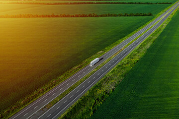 white truck driving on asphalt road along the green fields at sunset. seen from the air. Aerial view landscape. drone photography. cargo delivery