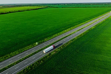 Abwaschbare Fototapete Grün Frachtlieferung. weißer LKW mit rotem Cockpit, das auf Asphaltstraße entlang der grünen Felder fährt. aus der Luft gesehen. Luftbild Landschaft. Drohnenfotografie.