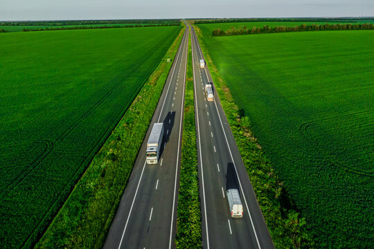 several white trucks on the higthway. cargo delivery driving on asphalt road along the green fields with goods. seen from the air. Aerial view landscape. drone photography. convoys with cargo