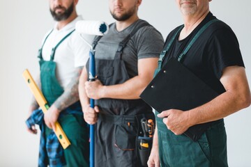 Crew of three professional builder wearing overalls standing in empty interior - obrazy, fototapety, plakaty