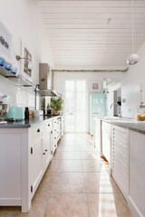 Bright kitchen interior with modern white furniture, pastel mint fridge and big floor to ceiling window