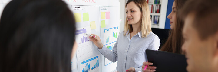 Woman coach standing at blackboard and showing documents with graphs to students