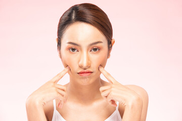 Unhappy Asian woman touching her cheek worry dry skin.Skin problem of beauty asian young woman having trouble of Dry skin, acne and wrinkles on pink background.Skin Problem Concept
