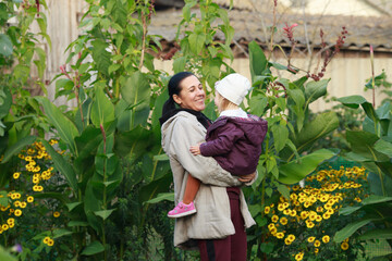 a brunette woman in a light jacket holds a little girl in her arms, looks at the child and smiles