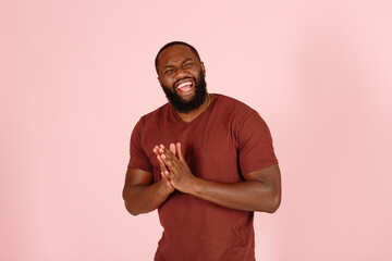 Joyful broadbrow young African-American man actor in casual brown t-shirt poses for camera on light pink background in studio - 459452615