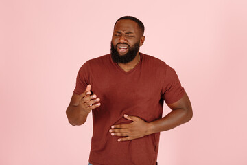 Young African-American man patient in t-shirt suffers from stomach ache standing on light pink background in studio closeup - 459452654