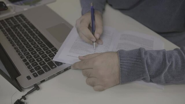 young man highlighting a book during the study near a laptop