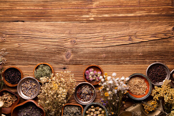 Natural medicine background. Assorted dry herbs in bowls and brass mortar on rustic wooden table.