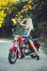 Plakat The biker is a beautiful cheerful girl sitting on her motorcycle, a little crazy. Wear short shorts and glasses. holding the steering wheel the wind blows the hair. Looks into the distance at the road