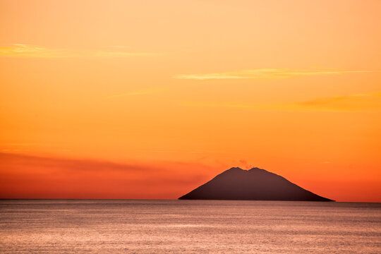 Stromboli active volcano against colorful sunset in Italy, view from Calabria coast.