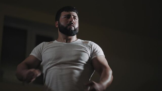 Low angle view of athletic power strong caucasian man showing his power and muscles in gym with dramatic lighting
