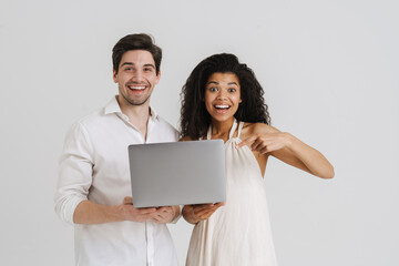 Multiracial excited couple holding and pointing finger at their laptop