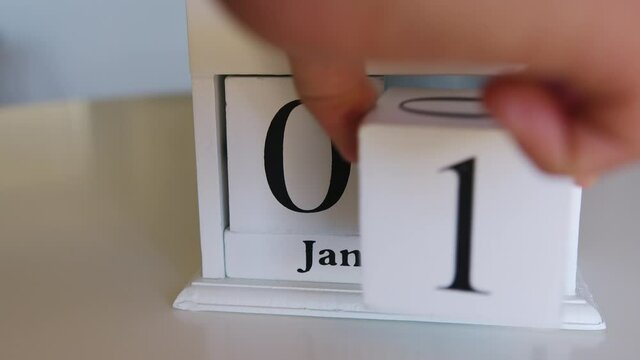 A white flip clock on table turns through month, flipping days and date. January 1st on the calendar.
