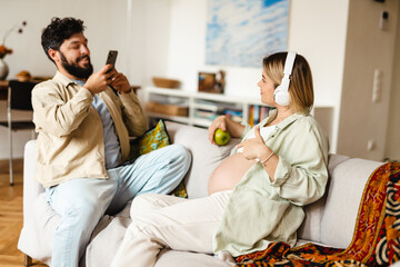 White man taking photo of his pregnant wife while sitting on couch
