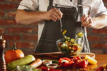 Cropped portrait of male chef, cook preparing vegetable salad in cafe, restaurant kitchen. Concept of a correct, healthy diet.