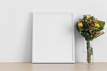 White frame mockup with a bouquet of roses on the wooden table.