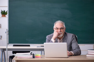 Old male teacher in front of blackboard