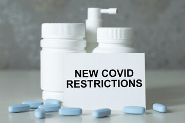 text new covid restrictions on paper next to scattered pills and medicine bottles, medical concept.