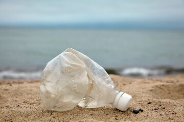 Crumpled plastic bottle on the sandy beach against the background of the sea