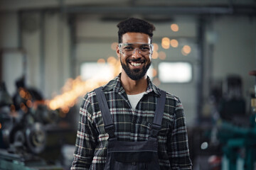 Portrait of young industrial man working indoors in metal workshop, looking at camera.