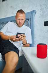 Male testing talking smart wireless speaker, man controlling home devices with a voice commands, sitting on sofa at home, Concept of smart home