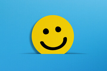 Happy smiley face emoticon coming out of a pocket on a blue background