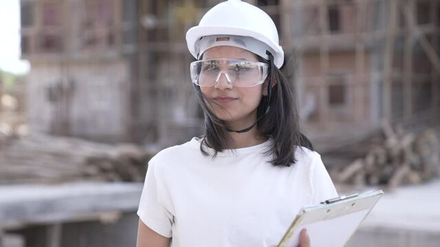 Portrait of Indian female industrial worker on construction site.Asian female industrial worker looking at camera wearing high vest and hard hat helmet or eyeglasses on outdoor.