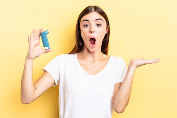 young hispanic woman looking surprised and shocked, with jaw dropped holding an object. asthma...
