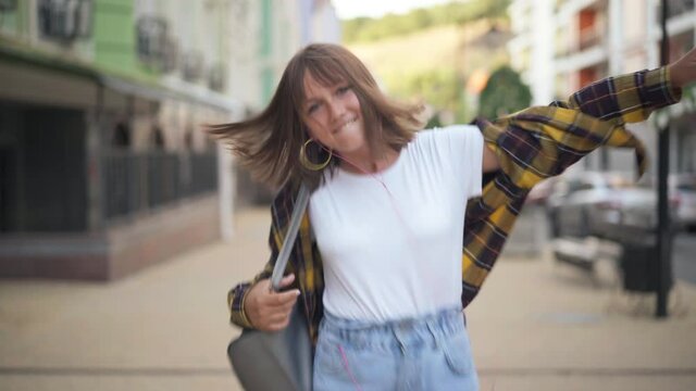 Portrait of joyful excited teenage girl dancing on city street walking listening to music in earphones. Happy carefree relaxed Caucasian teenager enjoying hobby outdoors in town. Joy and lifestyle