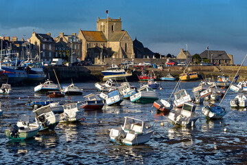Port at low tide at the end of the sunny day and church of Saint-Nicolas of Barfleur, a commune in the peninsula of Cotentin in the Manche departmentin Lower Normandy in north-western France - obrazy, fototapety, plakaty