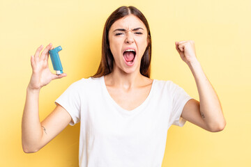 young hispanic woman shouting aggressively with an angry expression. asthma concept