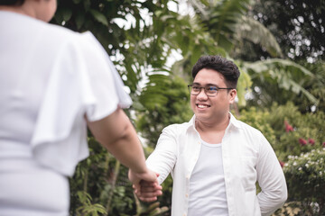 A smiling southeast asian asian guy in an unbuttoned white shirt takes his wife or fiancee's hand....