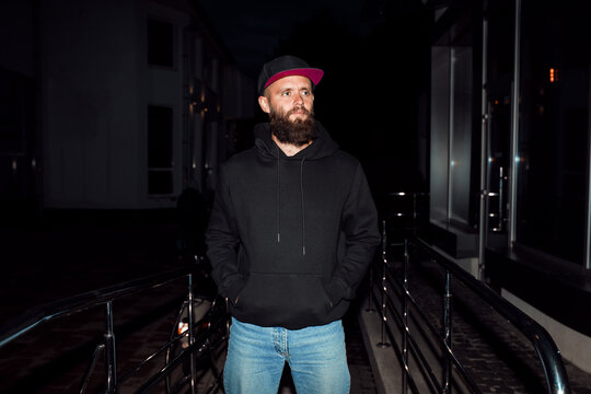 City portrait of handsome guy wearing black blank hoodie and baseball cap with space for your logo or design. Mockup for print