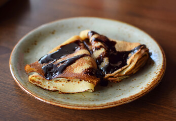 Crepes  are on a plate, drizzled with chocolate. Thin pancakes. Sweet dessert.