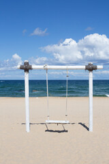 Swing on the seashore. White swing on the sandy beach.