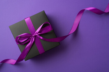 Top view photo of black giftbox with purple ribbon bow on isolated violet background with empty...