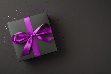 Above photo of black giftbox with purple ribbon wrapped as bow confetti and glitter around isolated...