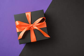 Top view photo of black giftbox with orange satin ribbon bow on isolated bicolor violet and black background with empty space