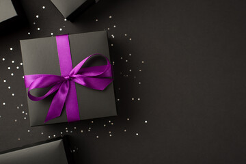 Top view photo of stylish black gift boxes with purple ribbon bow and sequins on isolated black background with copyspace