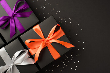 Top view photo of three black gift boxes with purple orange and white satin ribbon bows and sequins on isolated black background with copyspace