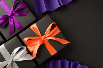 Top view photo of three black gift boxes with violet orange and white ribbon bows and violet paper fans on isolated black background with copyspace