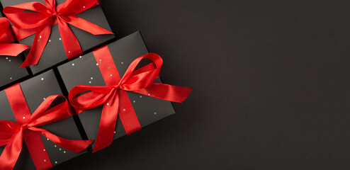 Top view photo of gift boxes in black packaging with sequins and red ribbon bow on isolated black...