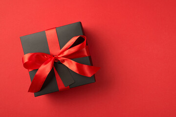 Top view photo of black giftbox with red ribbon bow and tag on isolated red background with blank space