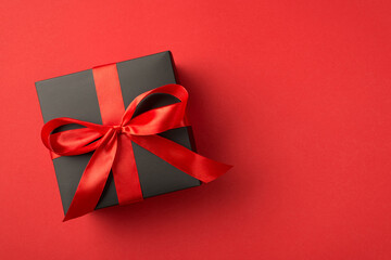 Top view photo of black giftbox with red ribbon bow on isolated red background with empty space